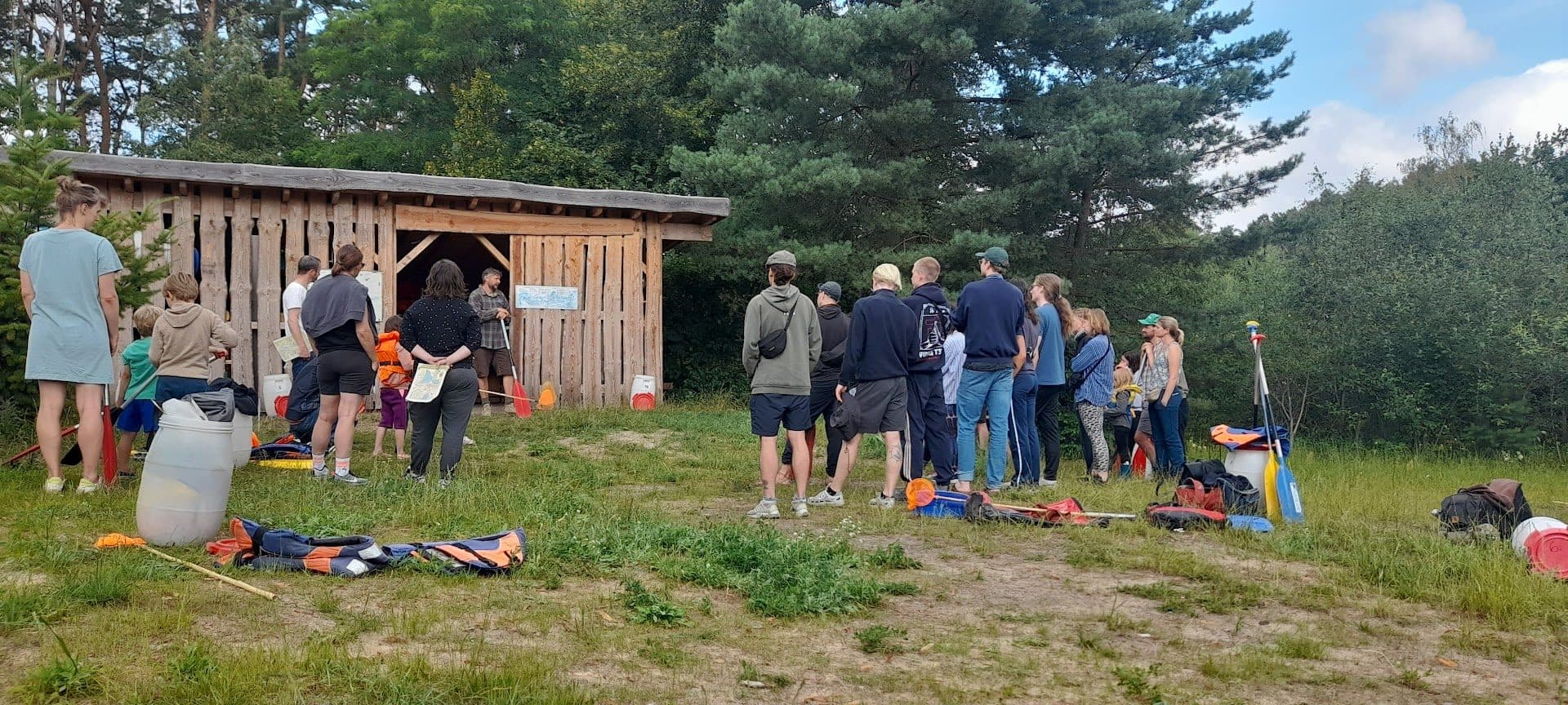 Eine Gruppe steht mit Paddeln vor dem hölzernen Unterstand