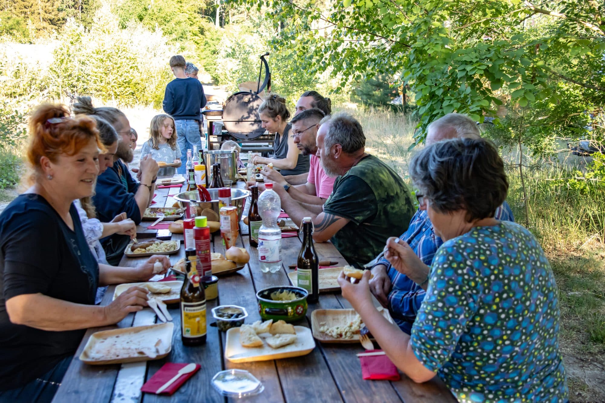 Gäste essen gemeinsam an einer langen Tafel im Freien