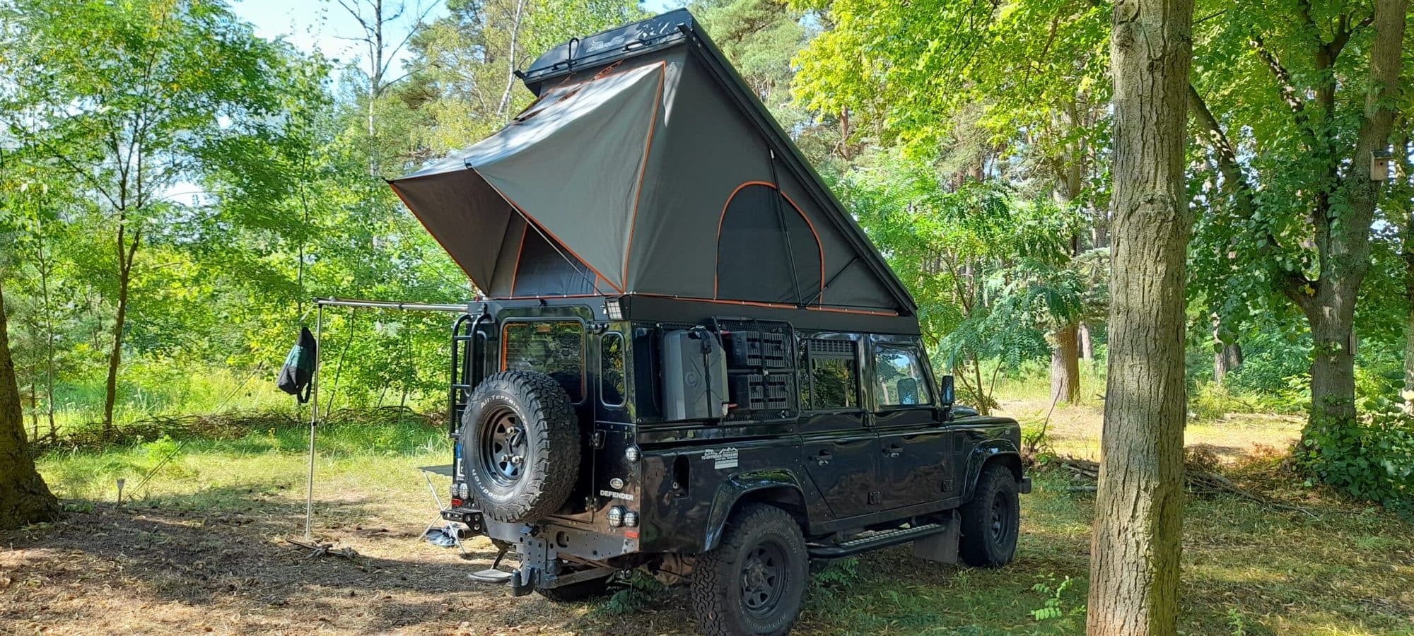 Geländewagen mit aufgestelltem Dachzelt zwischen Kiefern