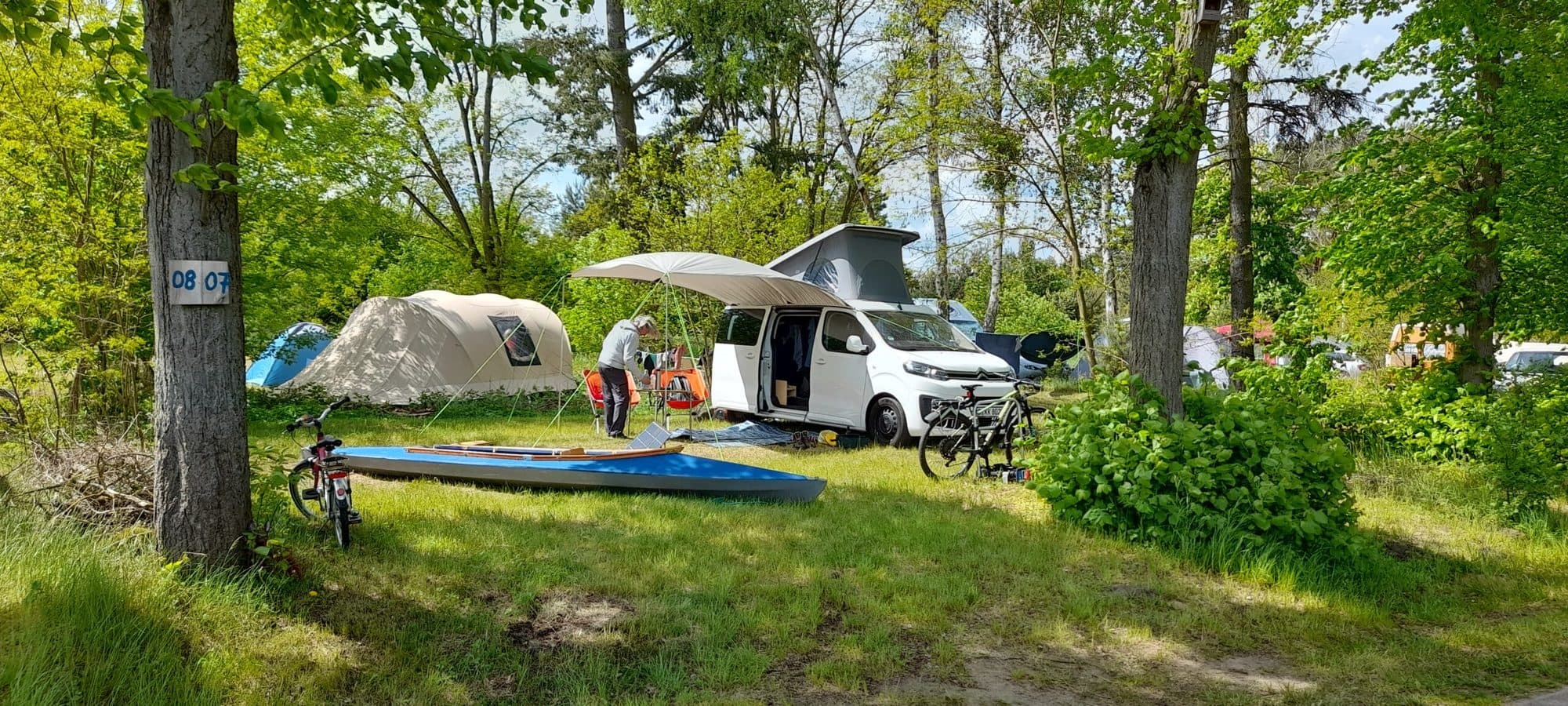 Van mit Dachzelt, davor ein Kanu auf der Wiese