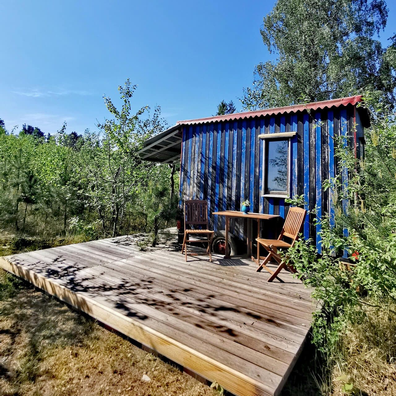 Zirkuswagen mit Holzveranda, davor Tisch und Stühle