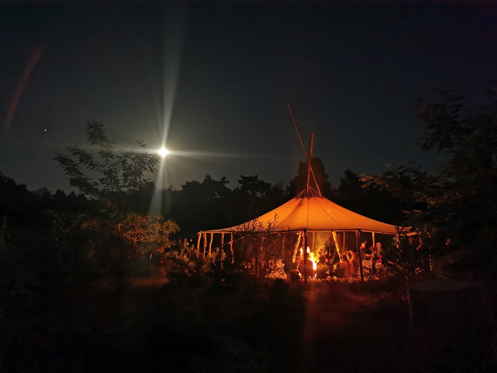 Beleuchtete Jurte mit Feuer davor, darüber der Vollmond