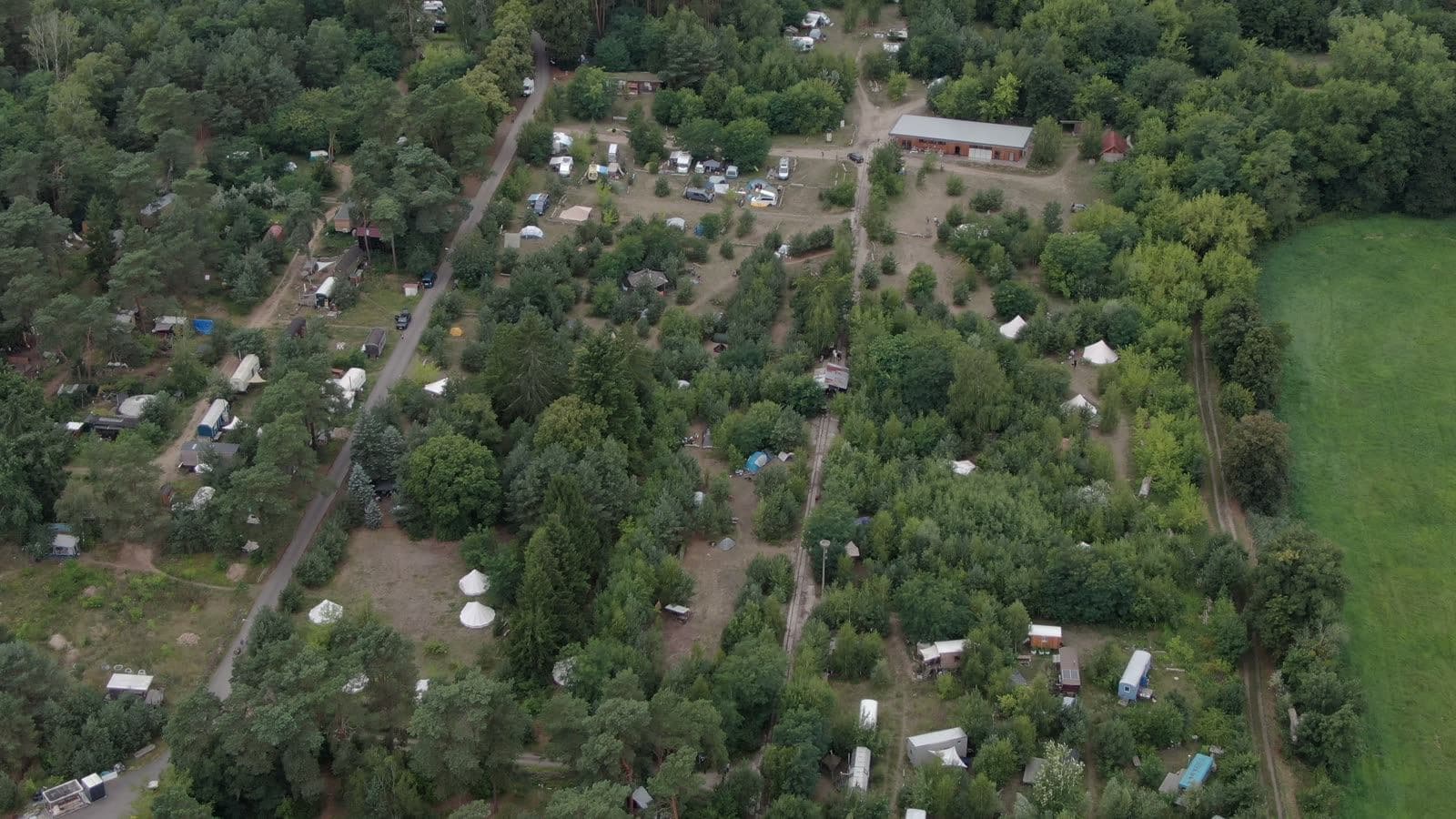Der Platz aus der Luft: Zelte und Wege zwischen Kiefern, dahinter Wald und Wiesen